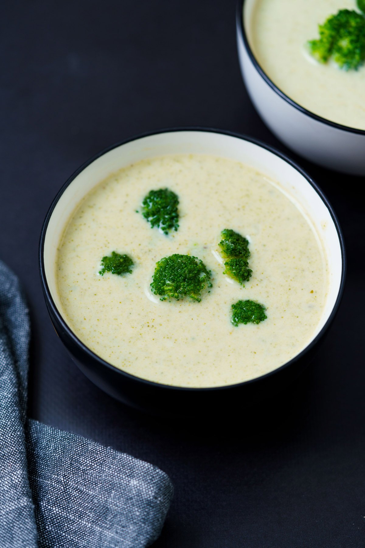 cream of broccoli soup topped with broccoli florets in a black rimmed white bowl on a black board