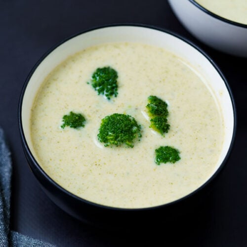 top shot of soup in black rimmed white bowl topped with three small broccoli florets
