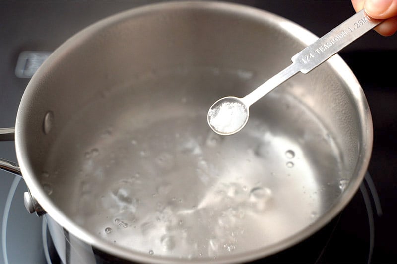 top shot of salt in teaspoon measuring spoon over pot of boiling water