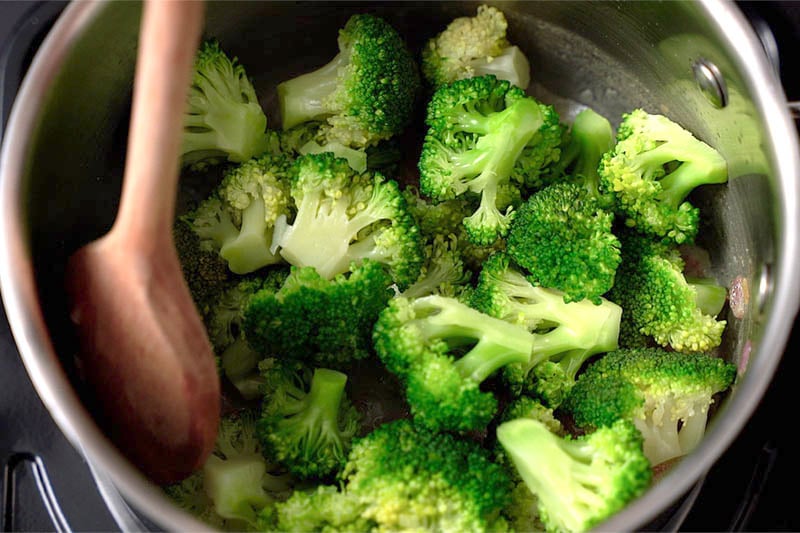 Top shot of wooden spoon stirring broccoli florets in pot