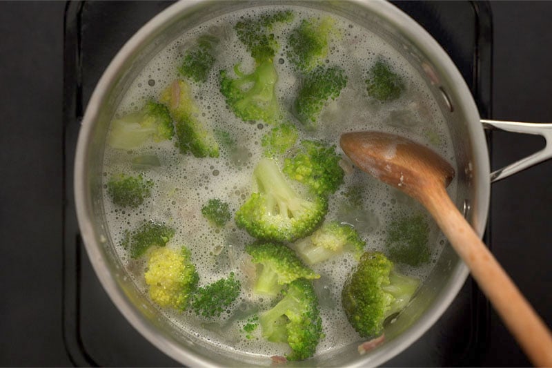 top shot of wooden spoon stirring broccoli soup mixture in pot