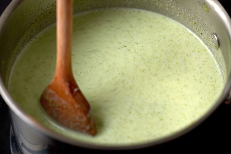 top shot of wooden spoon stirring milk into broccoli soup puree in pot