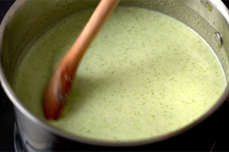 top shot of wooden spoon stirring cream of broccoli soup in pot