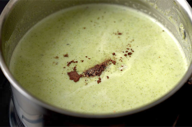 top shot of creamy broccoli soup with salt, ground black pepper and grated nutmeg added on the top in saucepan
