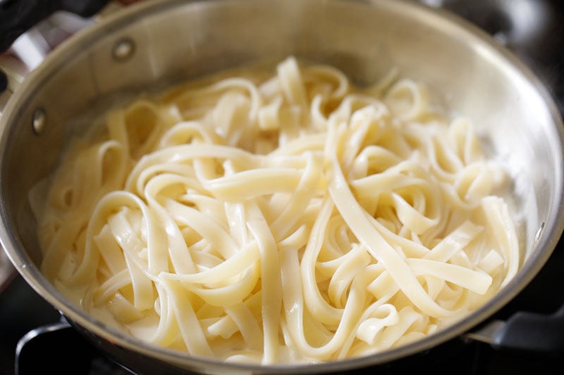 cooked al dente fettuccine pasta added to Alfredo sauce in pan