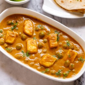 close up shot of matar paneer on white rectangle plate on white marble table