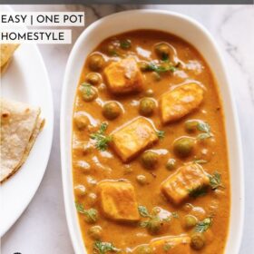 Top shot of matar paneer on white rectangle plate next to sliced cucumber in a white bowl and folded two roti in a white plate sitting on white marble table