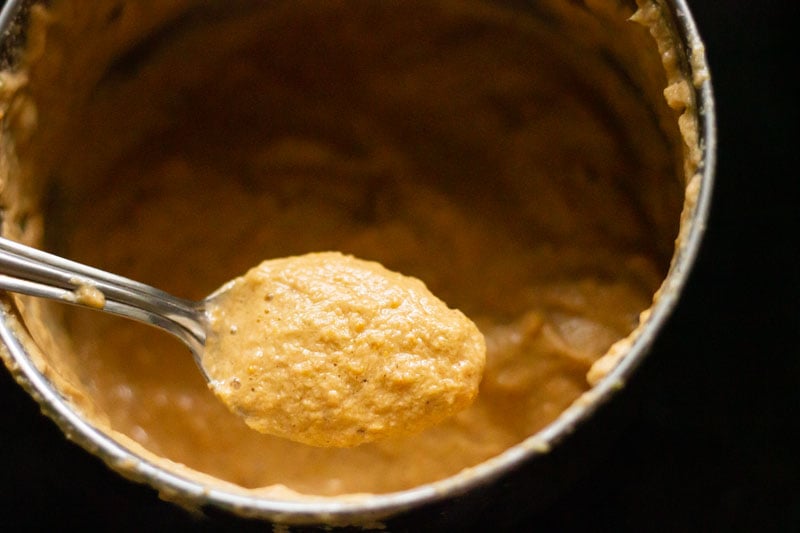 Spoon holding masala paste over the blender with ground paste