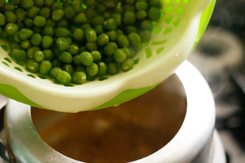 Green peas in green colander being added into pressure cooker