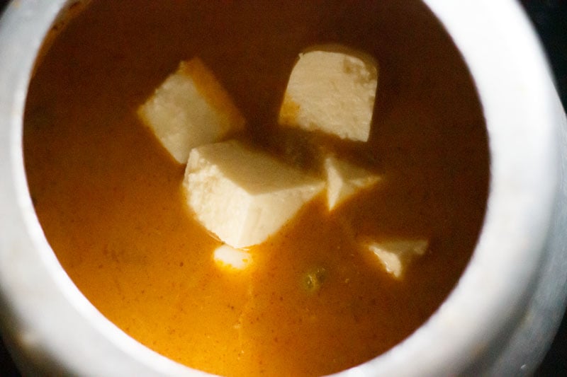 Top shots of paneer cubes in liquid masala and pea mixture, sitting in pressure cooker