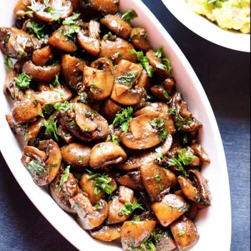 sautéed button mushrooms in an oblong white serving dish topped with fresh parsley