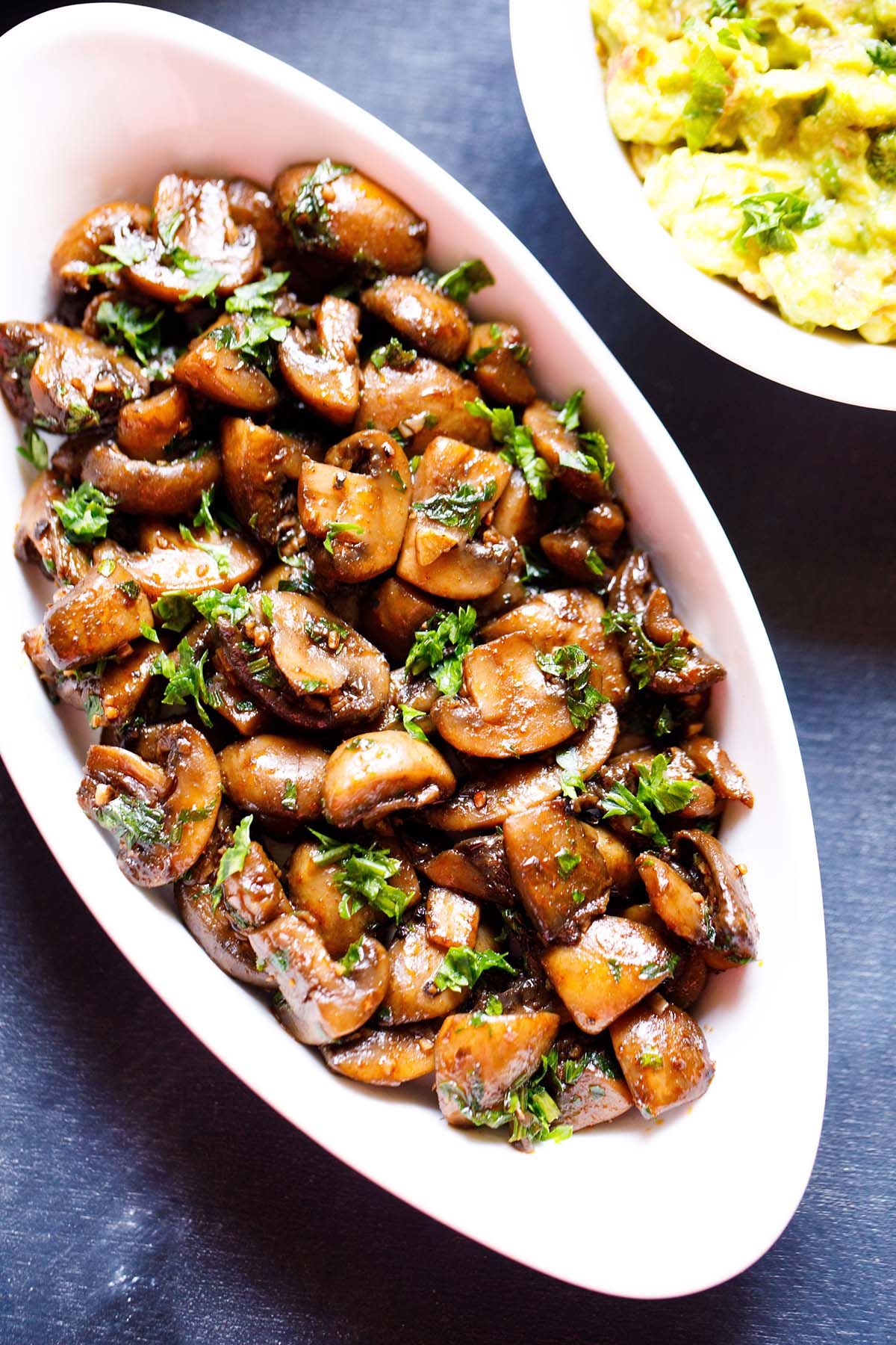 overhead shot of oblong white serving bowl filled with sautéed mushrooms and a side of guacamole