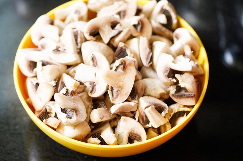 sliced button mushrooms in a yellow bowl