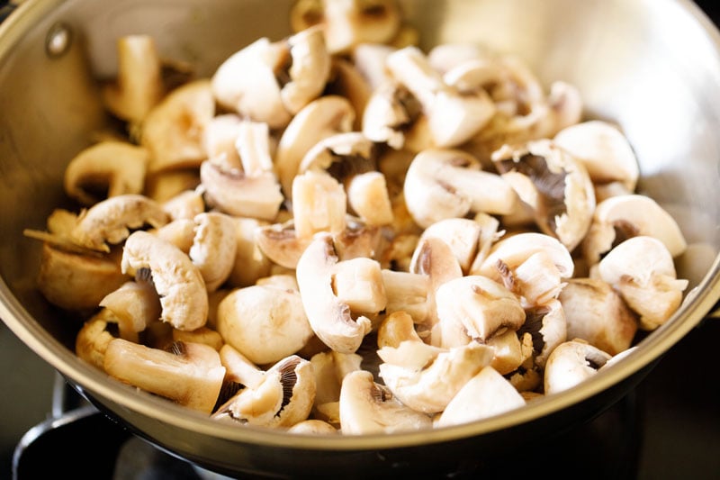 sliced raw button mushrooms added to skillet with garlic and oil