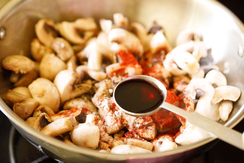 silver tablespoon full of red wine over skillet with mushrooms and seasonings