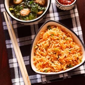 top shot of schezwan fried rice in a black rimmed triangular bowl with bamboo chopsticks at the side on a checkered black and white napkin