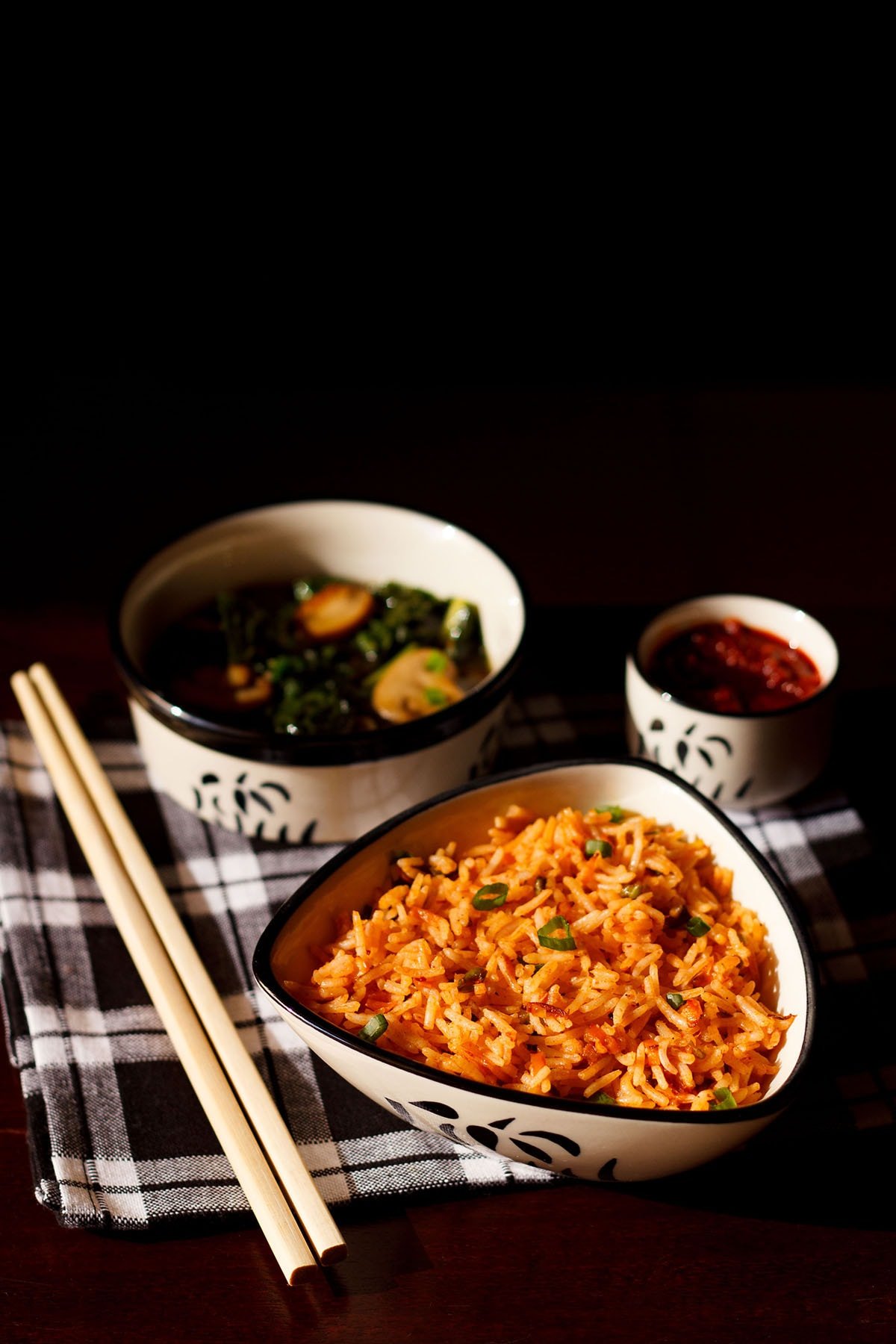 schezwan fried rice in a black and white triangular bowl with bamboo chopsticks at the side