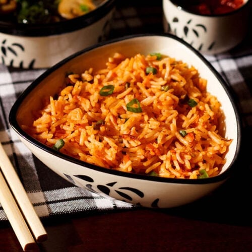 schezwan fried rice in a black and white triangular bowl with bamboo chopsticks at the side