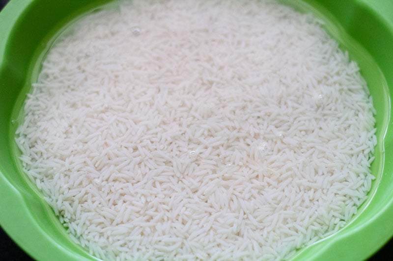 rice soaking in water in a green bowl to make schezwan fried rice