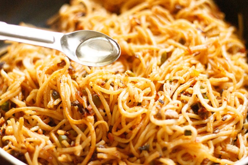 adding rice vinegar in a steel measuring spoon to the schezwan noodles