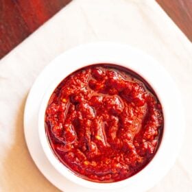 overhead shot of schezwan sauce in a white bowl placed on a white plate on a cream napkin