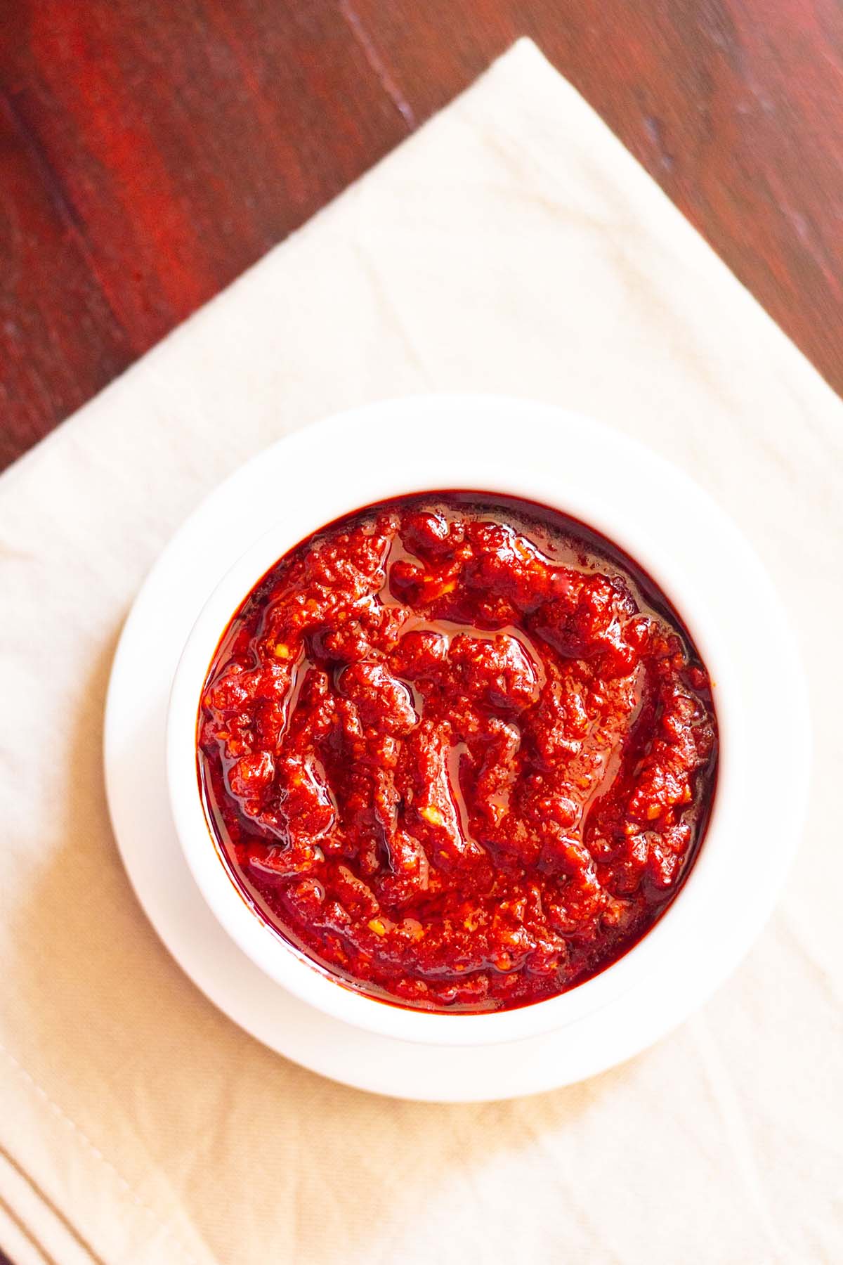 overhead shot of schezwan sauce in a white bowl placed on a white plate on a cream napkin