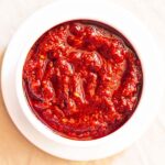 overhead shot of schezwan sauce in a white bowl placed on a white plate on a cream napkin