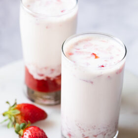 two collins glasses of strawberry milk with the back glass showing the strawberry syrup at the bottom of the glass