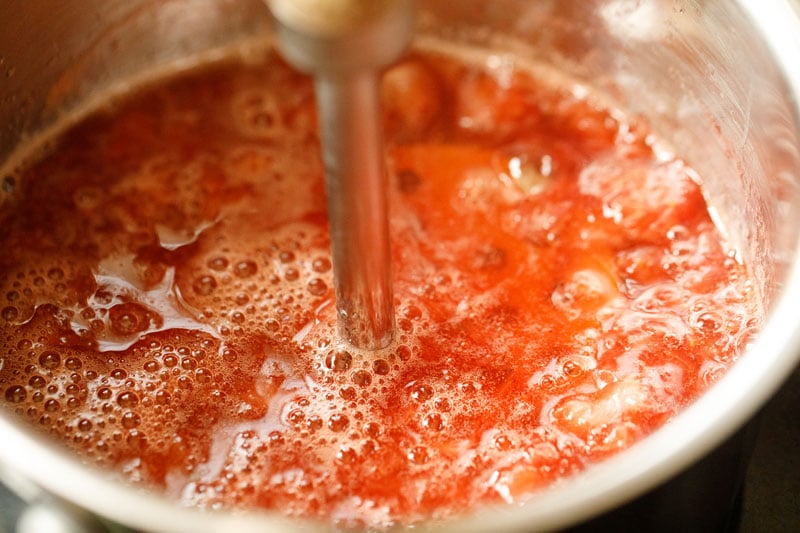 masher in saucepan with strawberry syrup