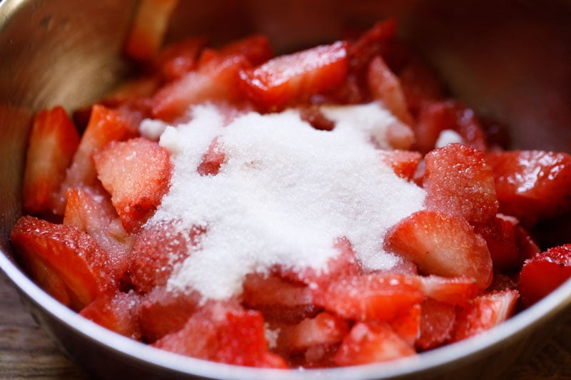 chopped strawberries topped with castor sugar in a steel mixing bowl