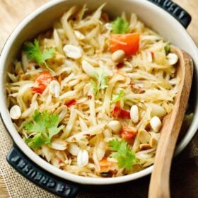 thai green papaya salad garnished with fresh cilantro and roasted peanuts in a black le creuset dish with a wooden spoon