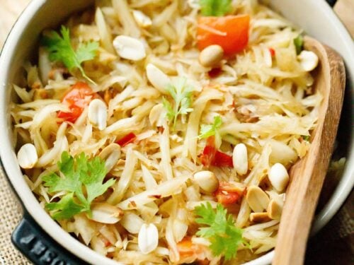 thai green papaya salad garnished with fresh cilantro and roasted peanuts in a black le creuset dish with a wooden spoon