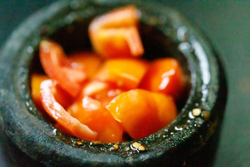 tomatoes added to mortar with som tam dressing ingredients