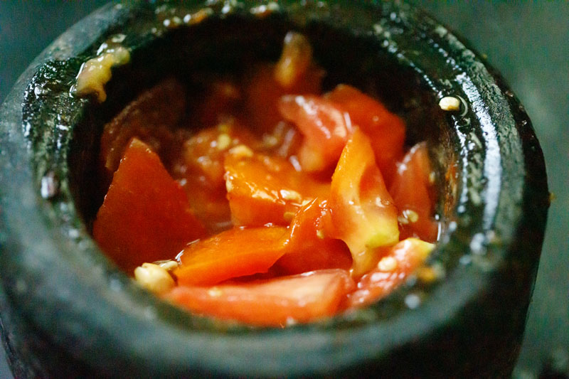 lightly mashed tomatoes in mortar with green papaya salad dressing