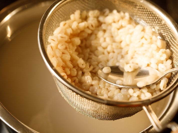 spoon pressing barley through a mesh strainer