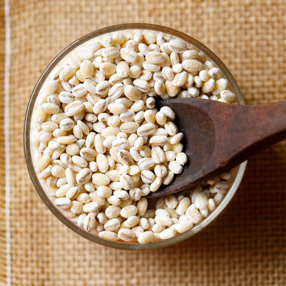 small glass bowl. of pearled barley on a piece of burlap with a wooden spoon