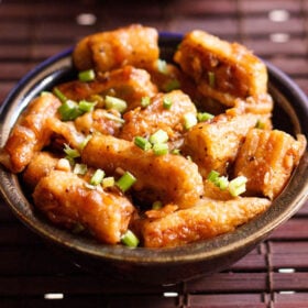 chilli baby corn garnished with spring onion greens in a dark brown ceramic bowl