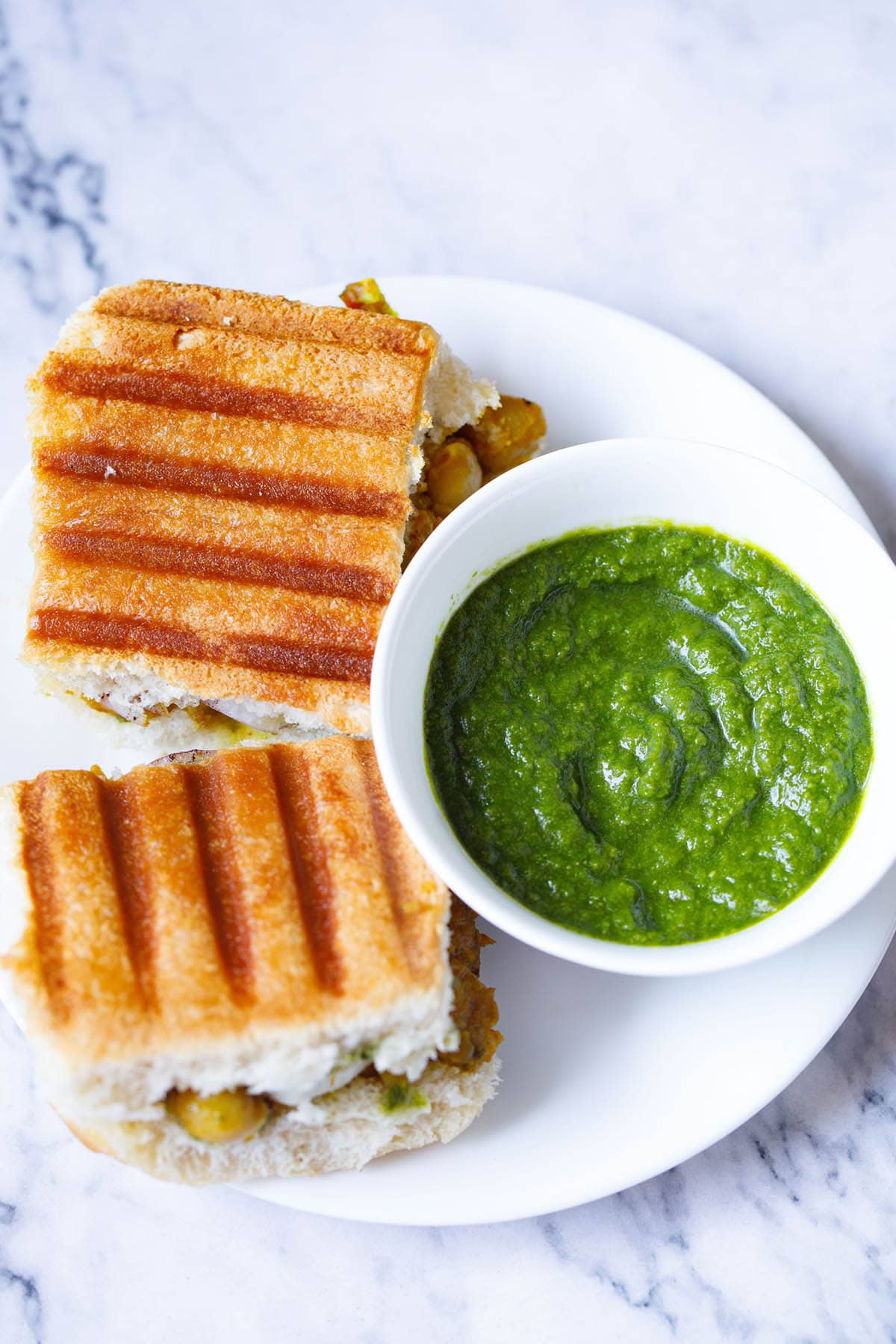 cilantro chutney in white bowl placed next to grilled sandwiches on a white plate