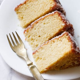 close up shot of thick slices of eggless vanilla cake on a square shaped white plate woth a brass fork on the plate