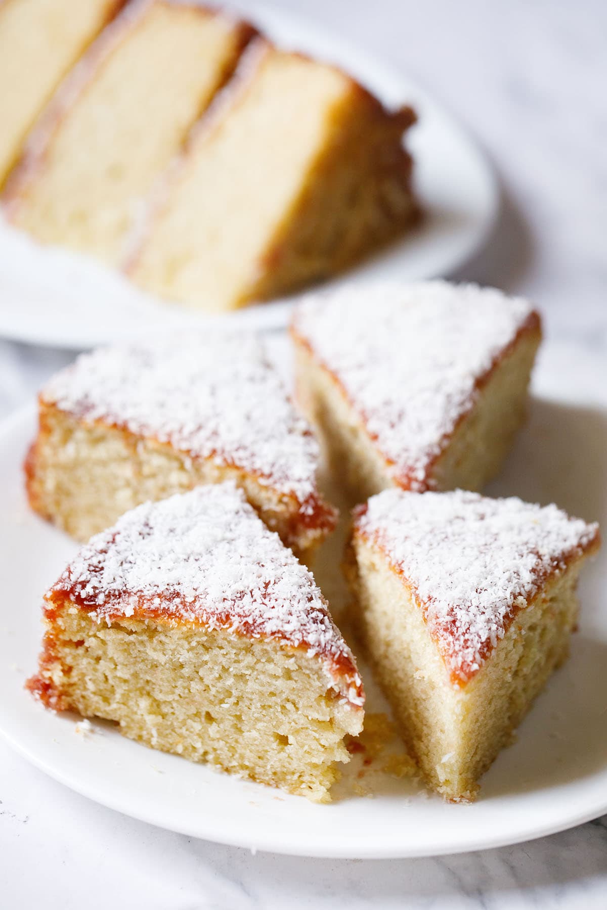 vanilla cake triangular wedges topped with jam icing and desiccated coconut on a white plate