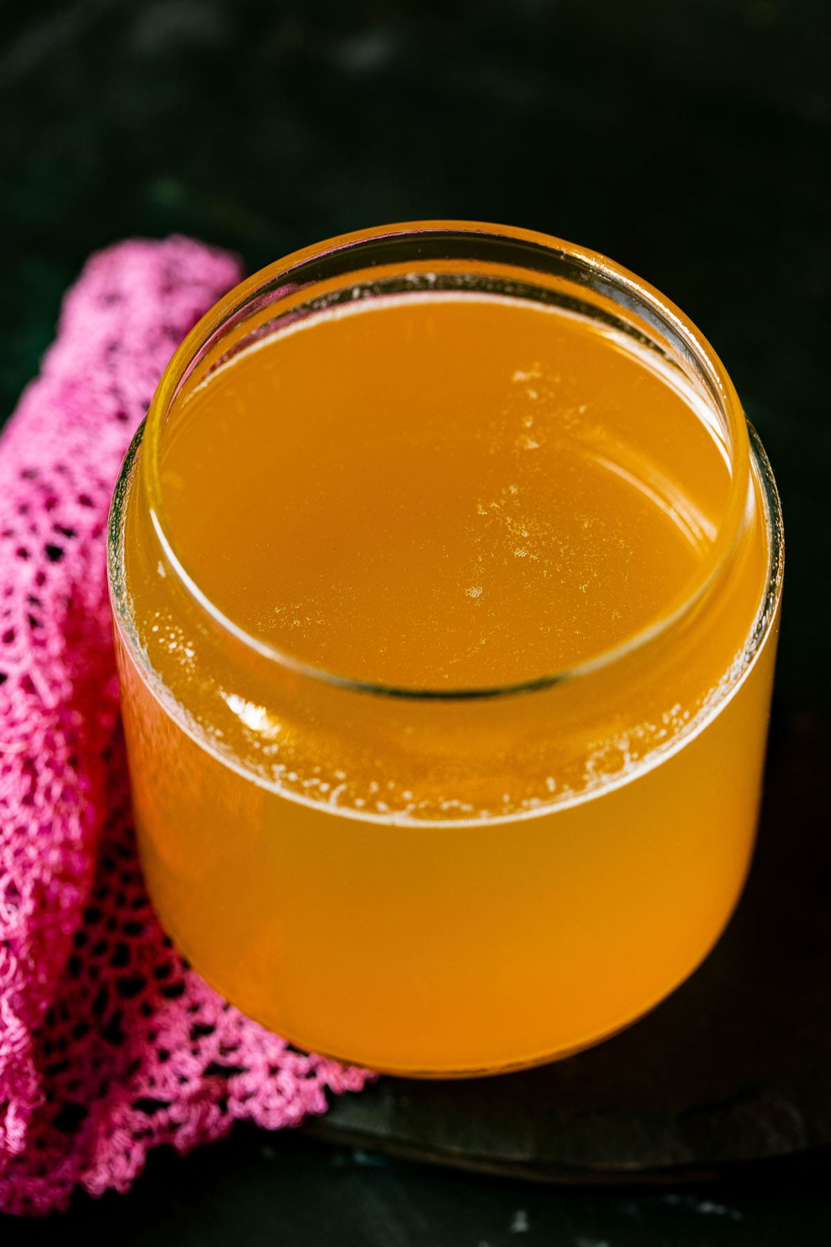 clear liquid ghee in a glass jar with a dark pink doily by the side on a black surface