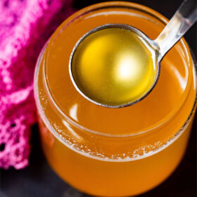 clear can shaped glass filled with golden ghee and a small silver ladle removing some