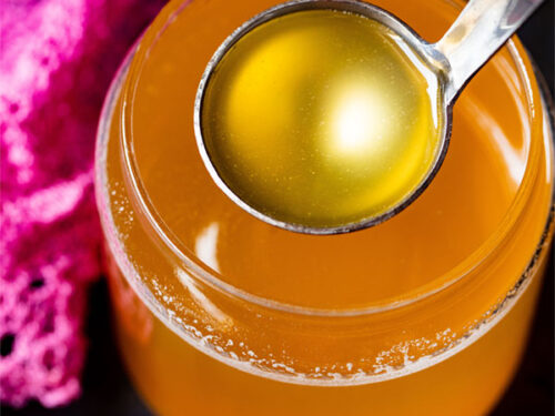 clear can shaped glass filled with golden ghee and a small silver ladle removing some