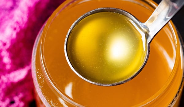 clear can shaped glass filled with golden ghee and a small silver ladle removing some