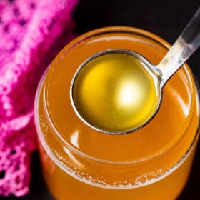 clear can shaped glass filled with golden ghee and a small silver ladle removing some