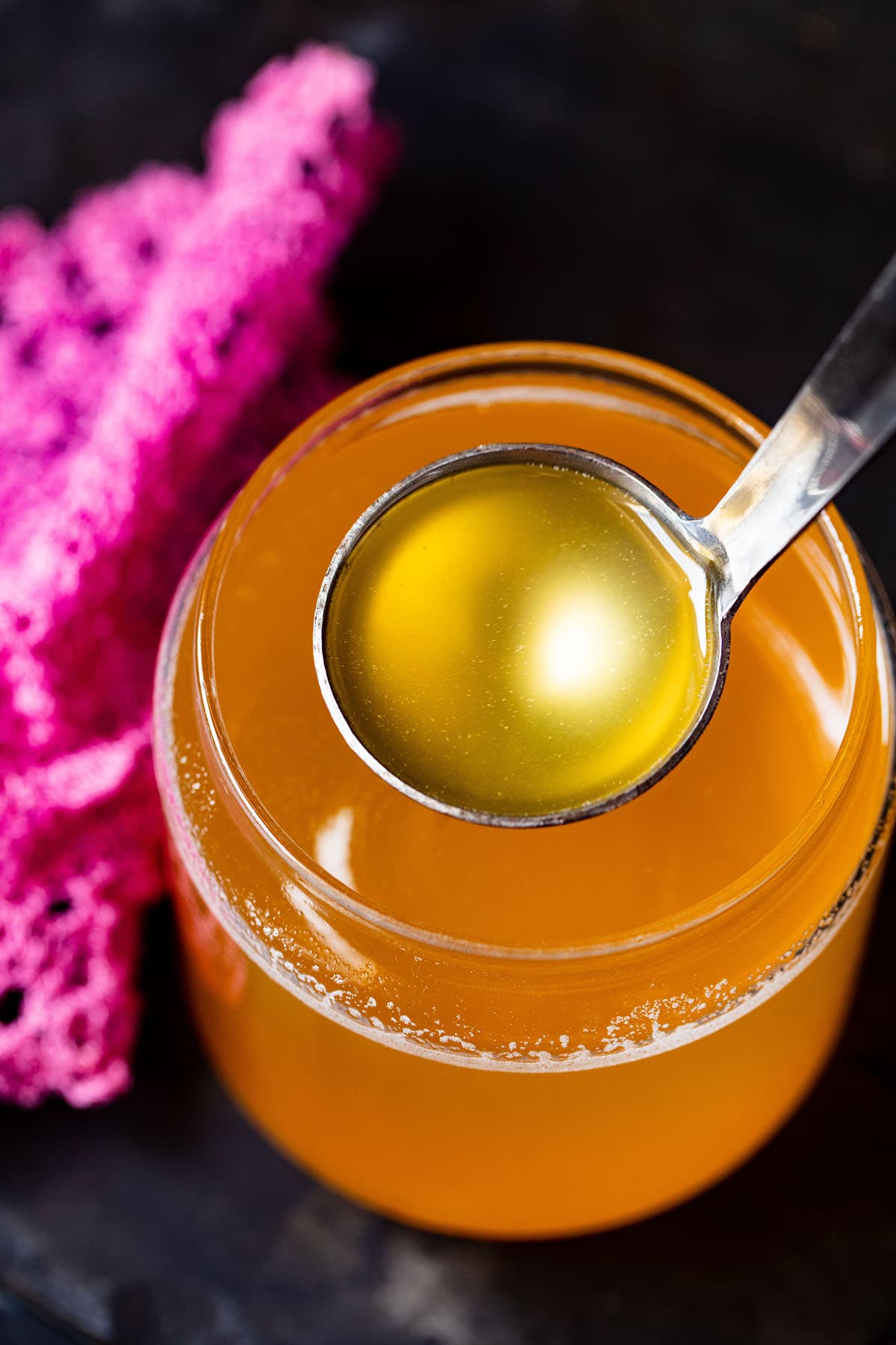 clear can shaped glass filled with golden ghee and a small silver ladle removing some