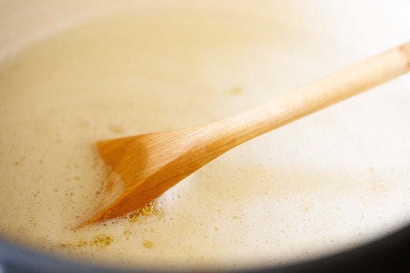 wooden spoon stirring simmering butter to make ghee