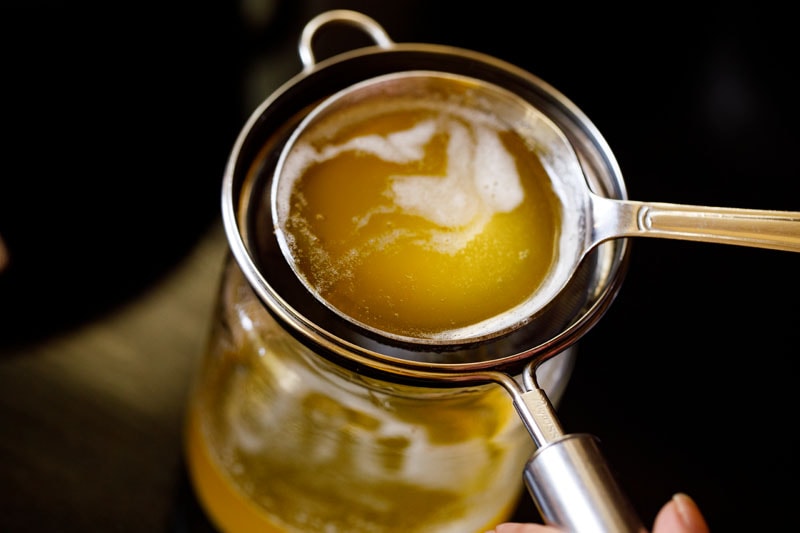 ladle pouring ghee through a strainer into a glass jar