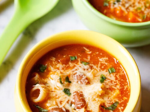 overhead shot of vegetable minestrone soup in a yellow bowl garnished with parmesan cheese and fresh basil