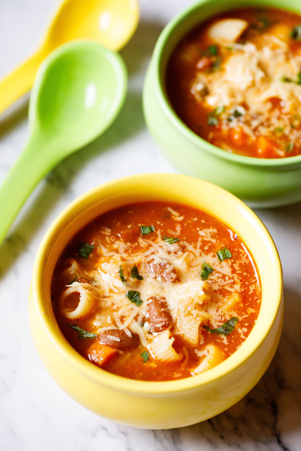 overhead shot of vegetable minestrone soup in a yellow bowl garnished with parmesan cheese and fresh basil